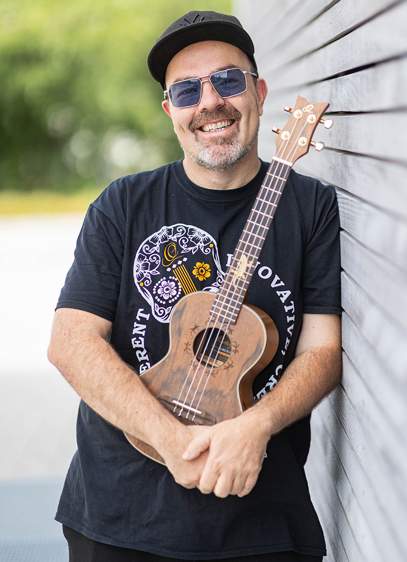 Rüdiger Eisenhauer stehend an einer Wand lehnend mit einer Ukulele in den Händen